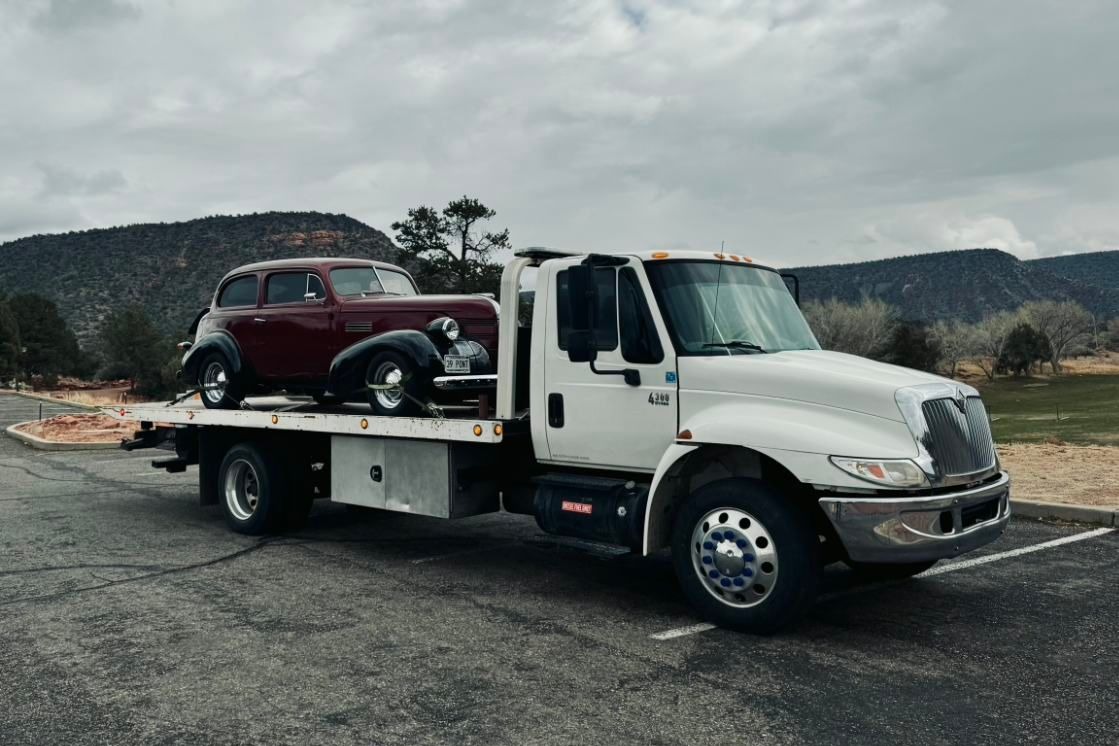 A dark red vintage car loaded and secured for transport on the deck of an open trailer