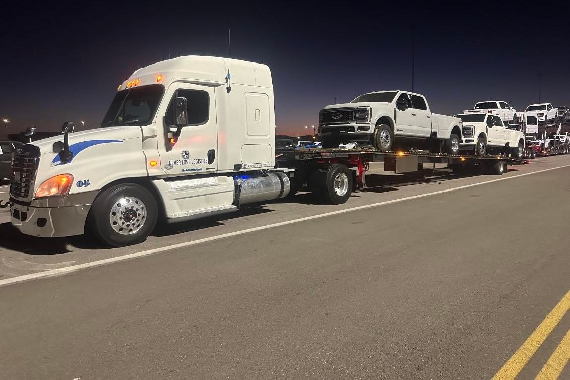 A Never Lost Logistics tractor and loaded open trailer on the road at dusk