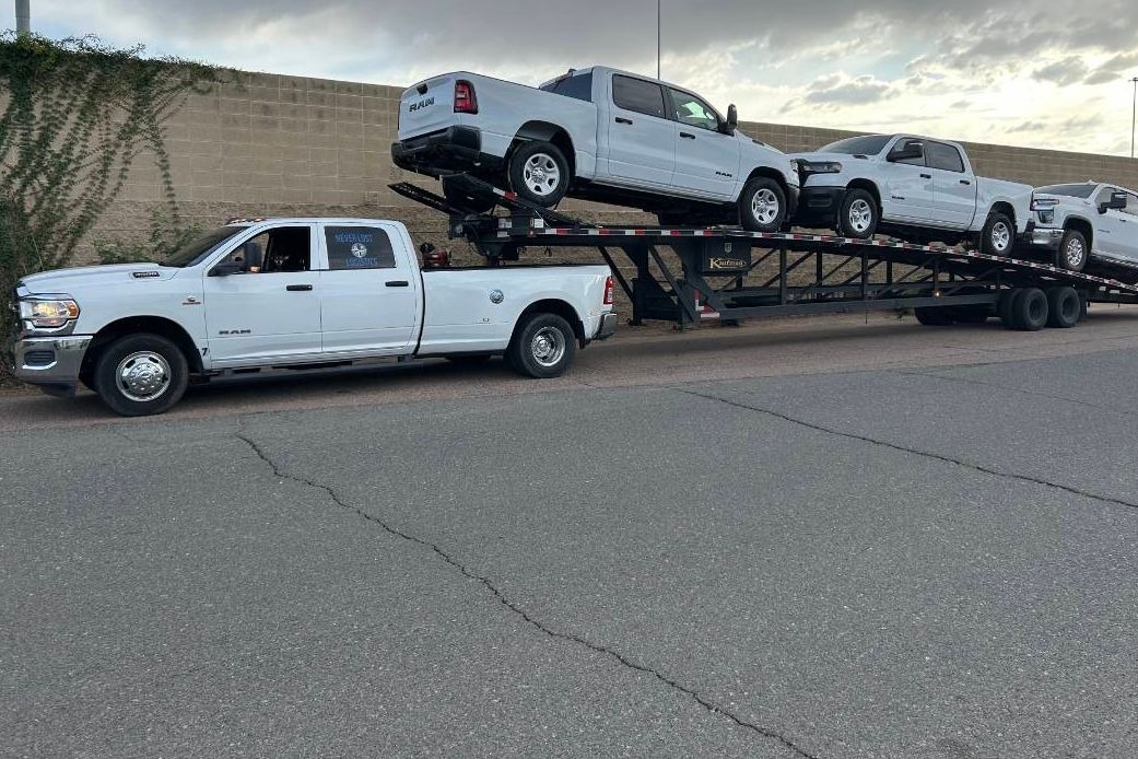 A heavy-duty pickup and gooseneck trailer loaded with three trucks, ready for a long haul