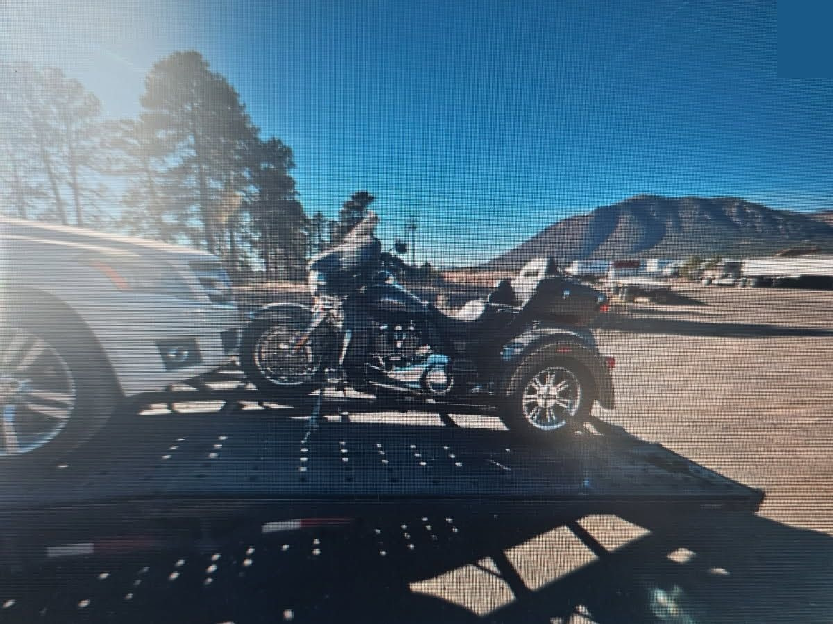 A black three-wheeled motorcycle strapped down at both ends on the Never Lost Logistics open transport trailer