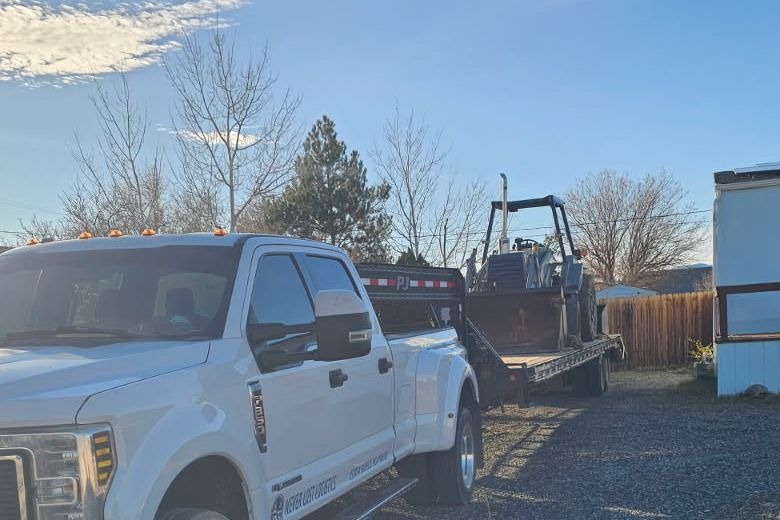 A white dually pickup hitched to an open utility trailer loaded with a small excavator