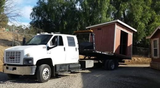 A small red wooden shed strapped down and secured on an open transport deck